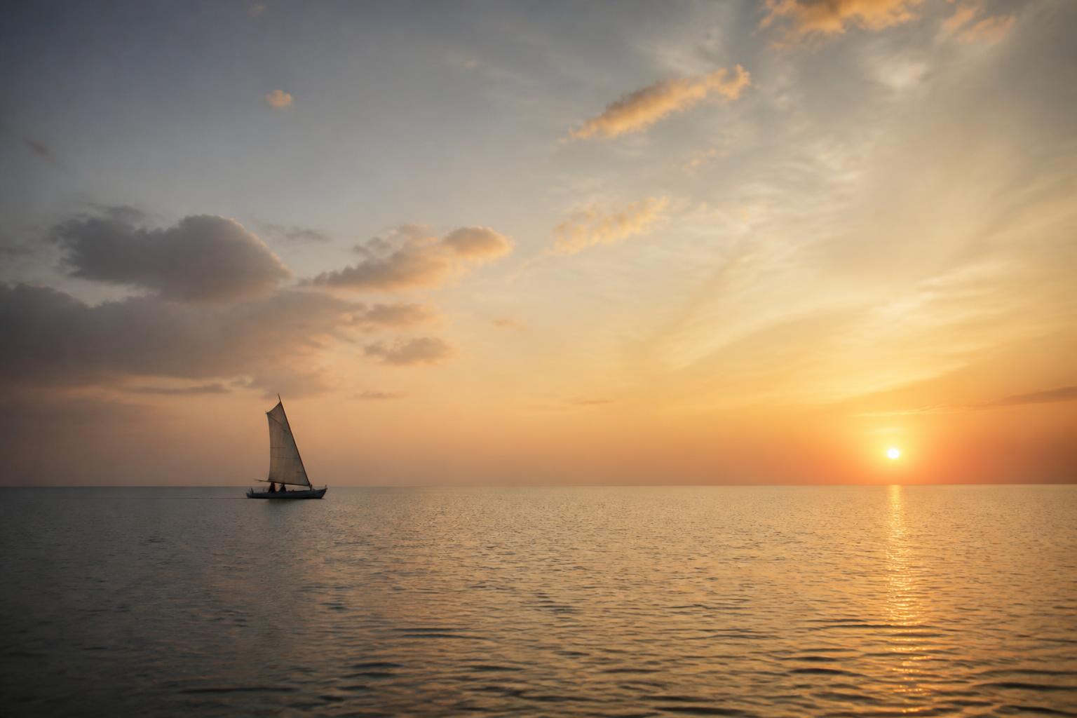 A single sailboat on a calm sea at dawn — direction in a vast world.